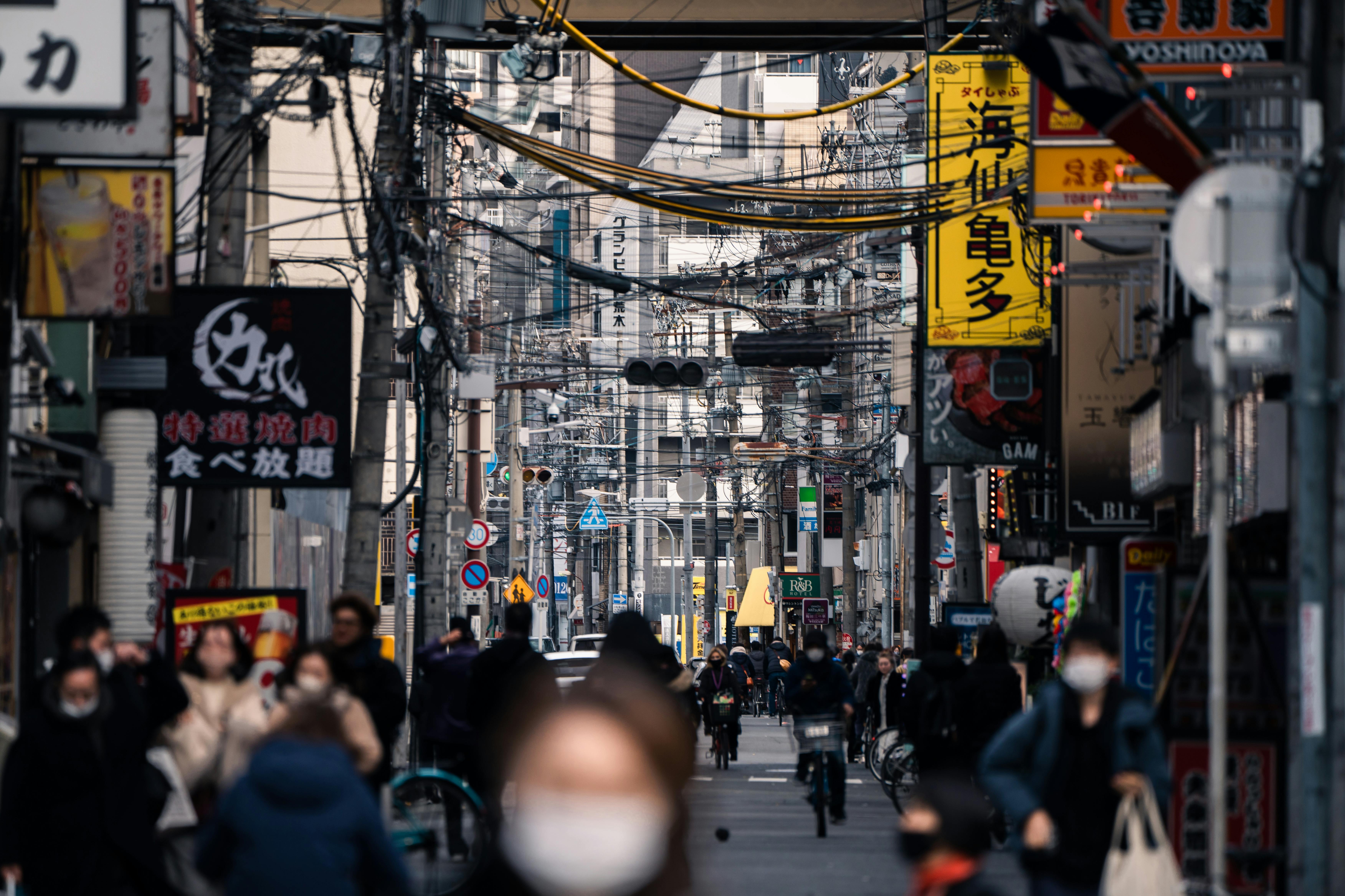 Crowded street in Osaka, Japan bustling with masked pedestrians and vibrant advertising signs.