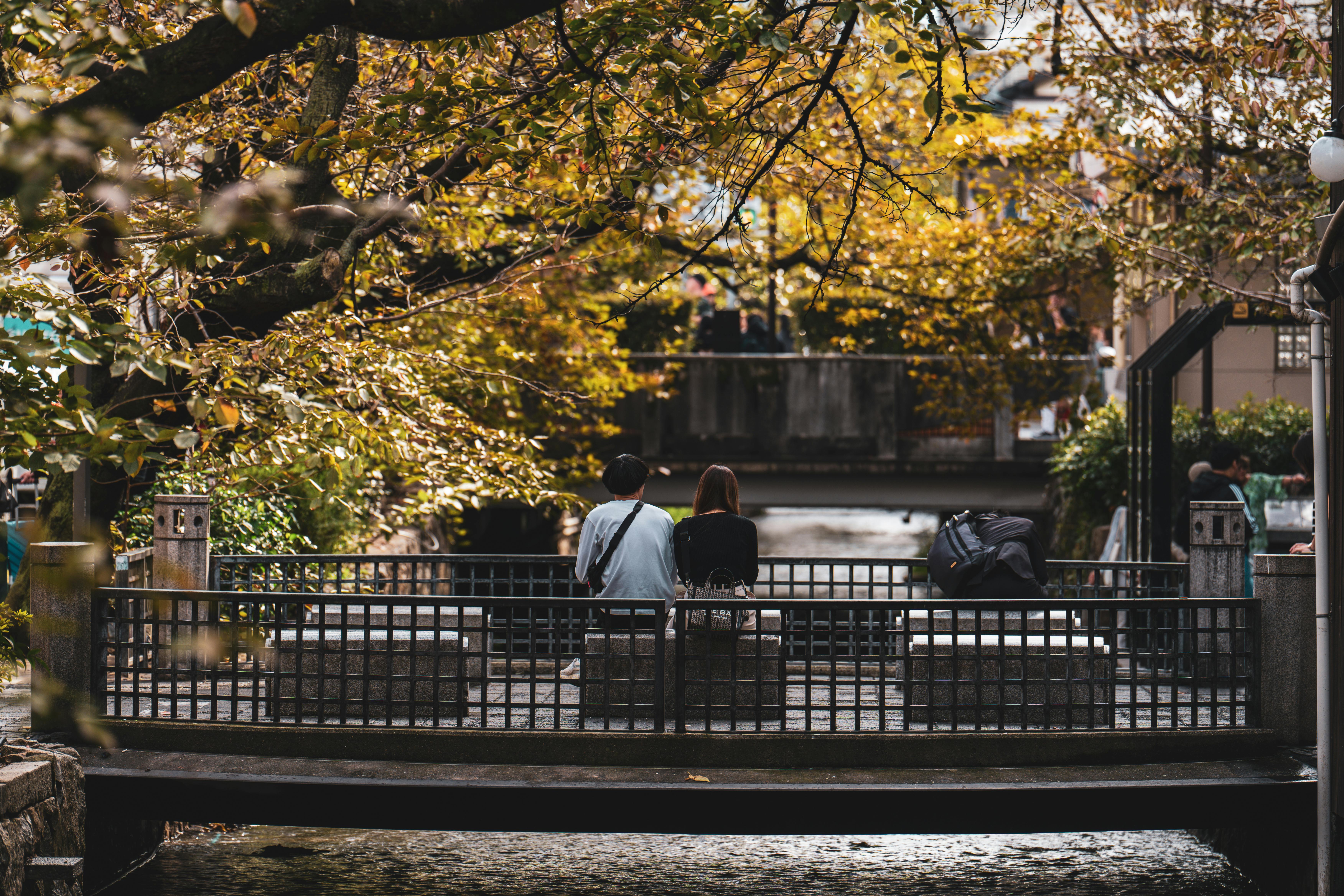 A couple relaxes on a serene bridge in Kyoto, Japan, during a vibrant autumn day.