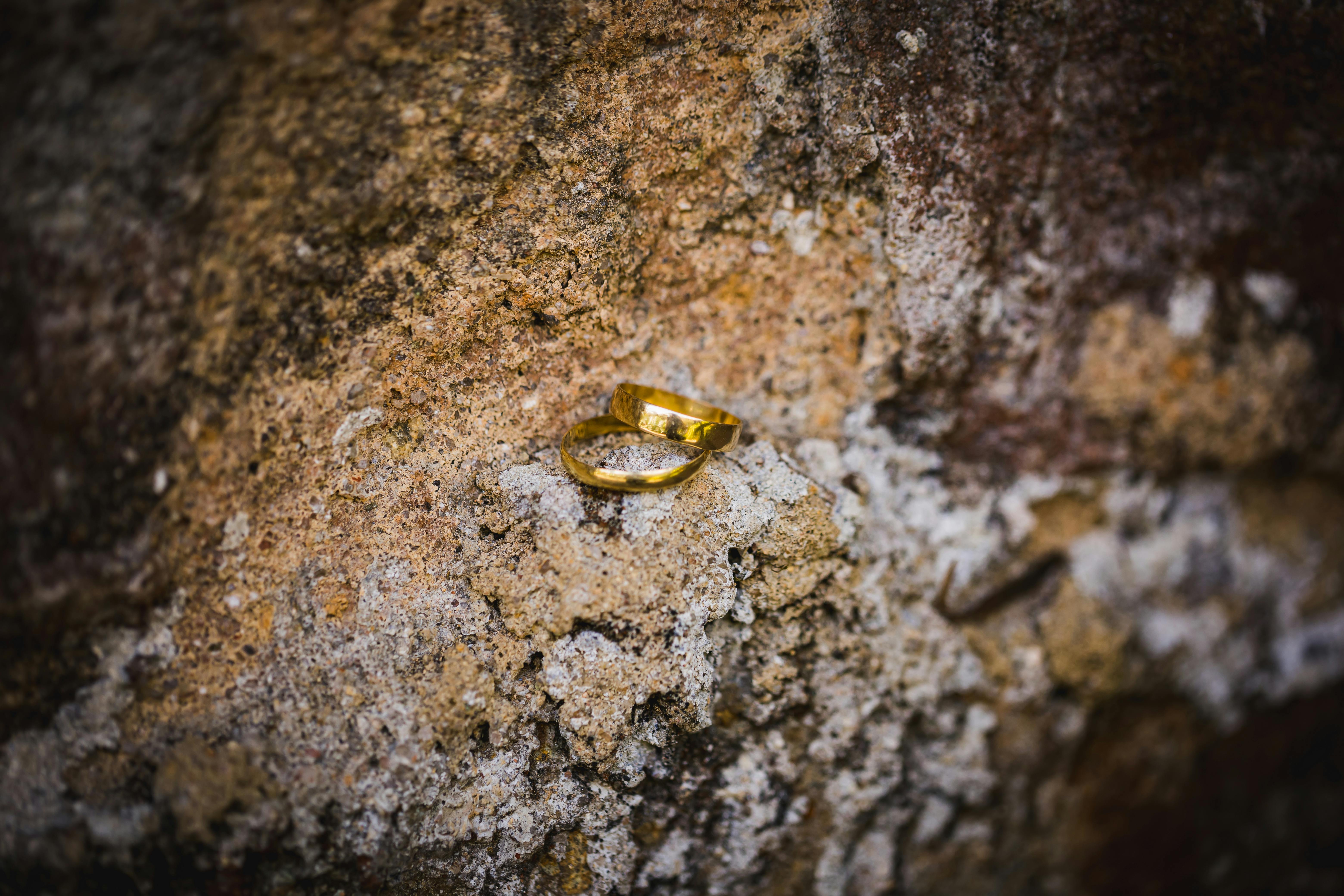 Close-up of gold wedding rings placed on a textured stone, symbolizing love and commitment.