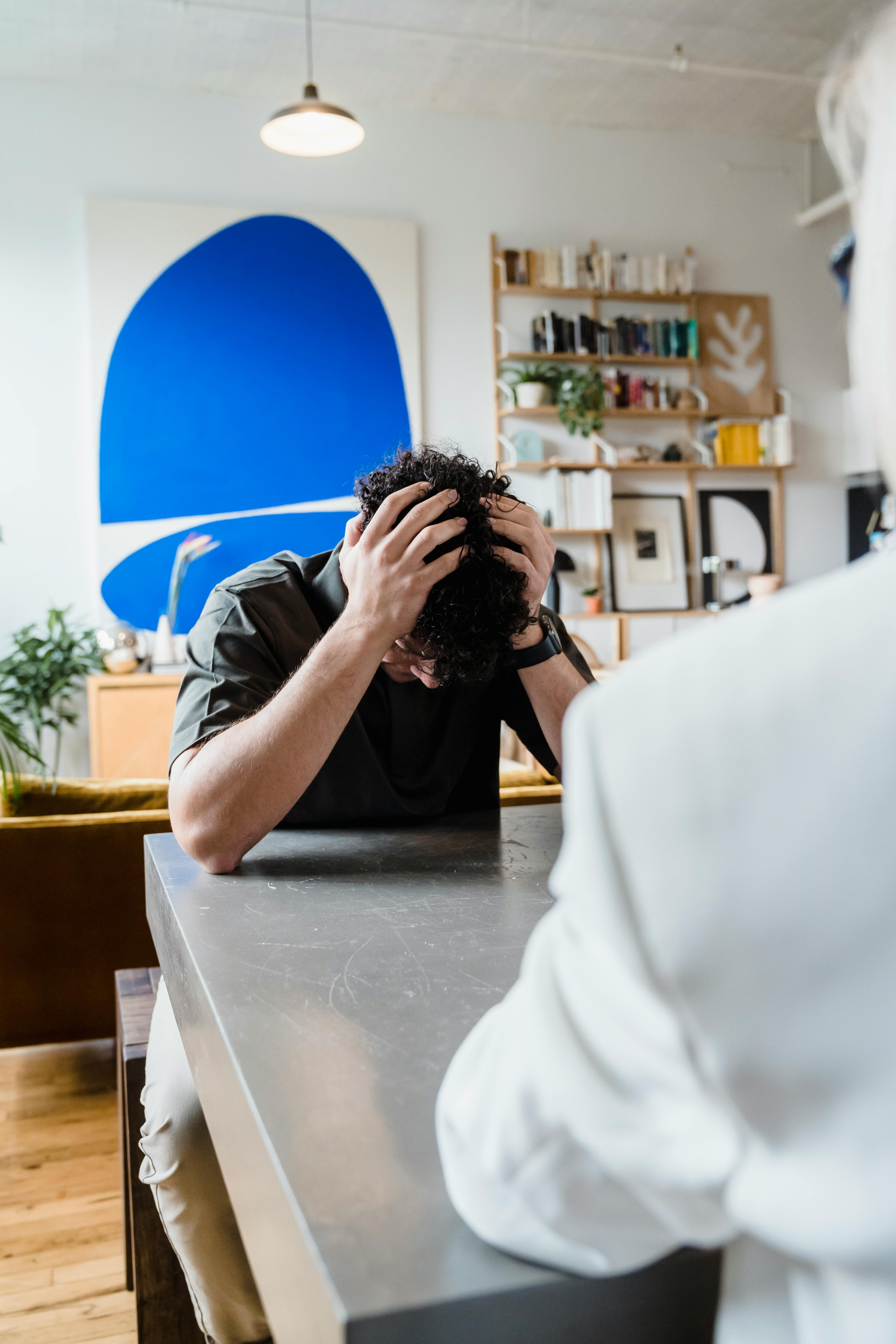 Young adult facing emotional stress in a modern living room setting, head in hands.