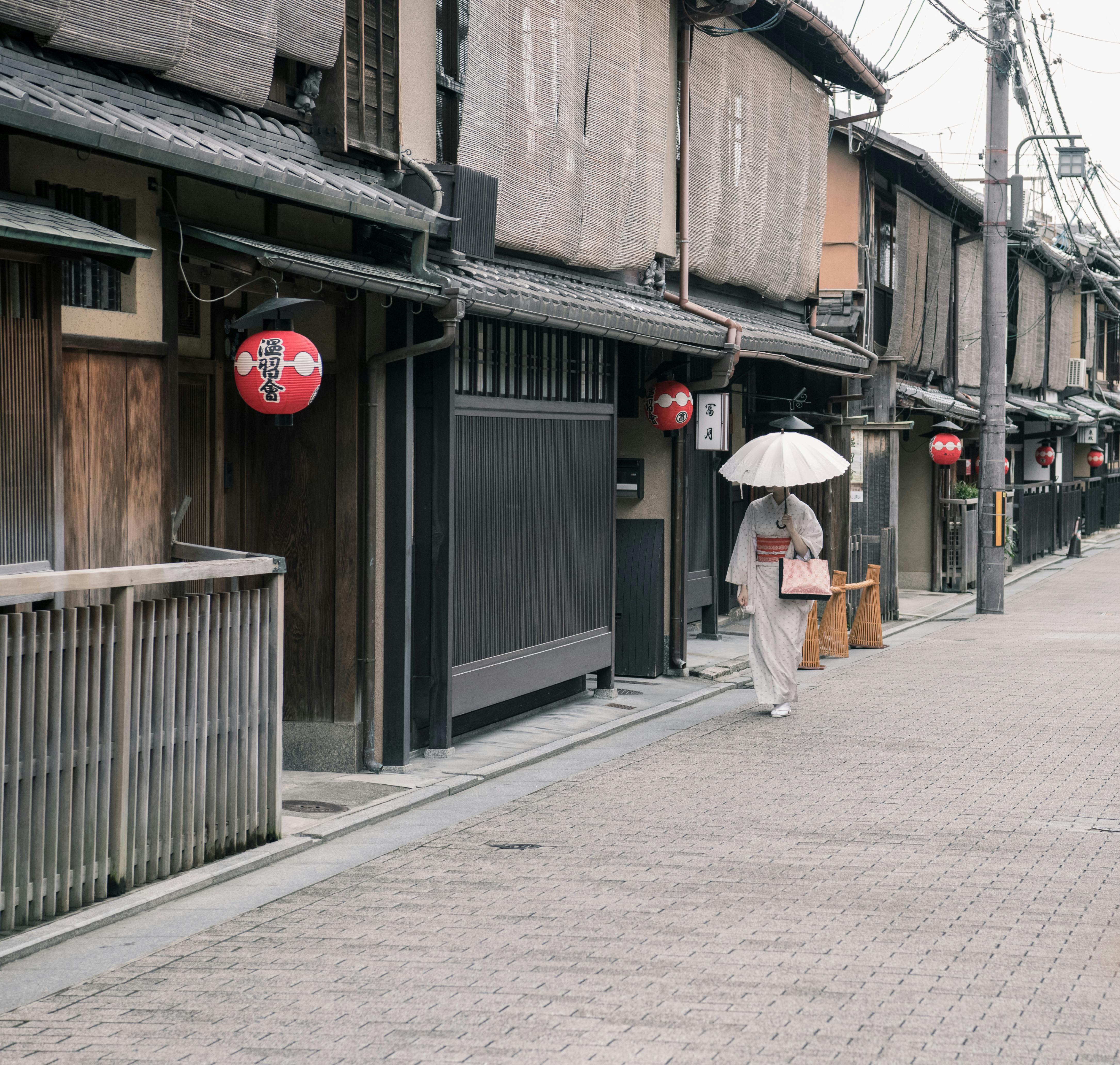 A woman in a kimono walks down a traditional street in Kyoto, Japan, holding an umbrella.