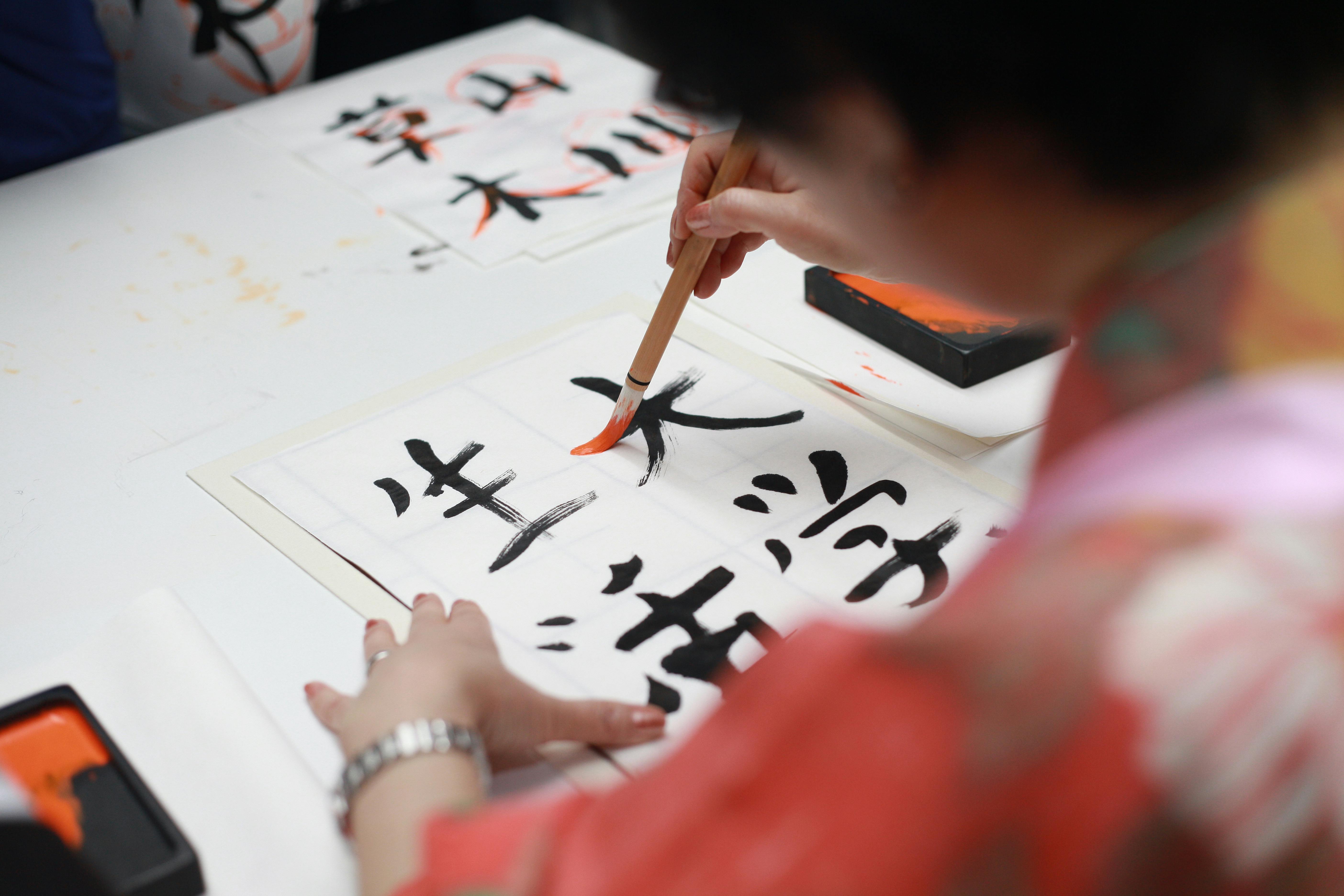 Close-up of a person practicing traditional Japanese calligraphy with a brush on paper.