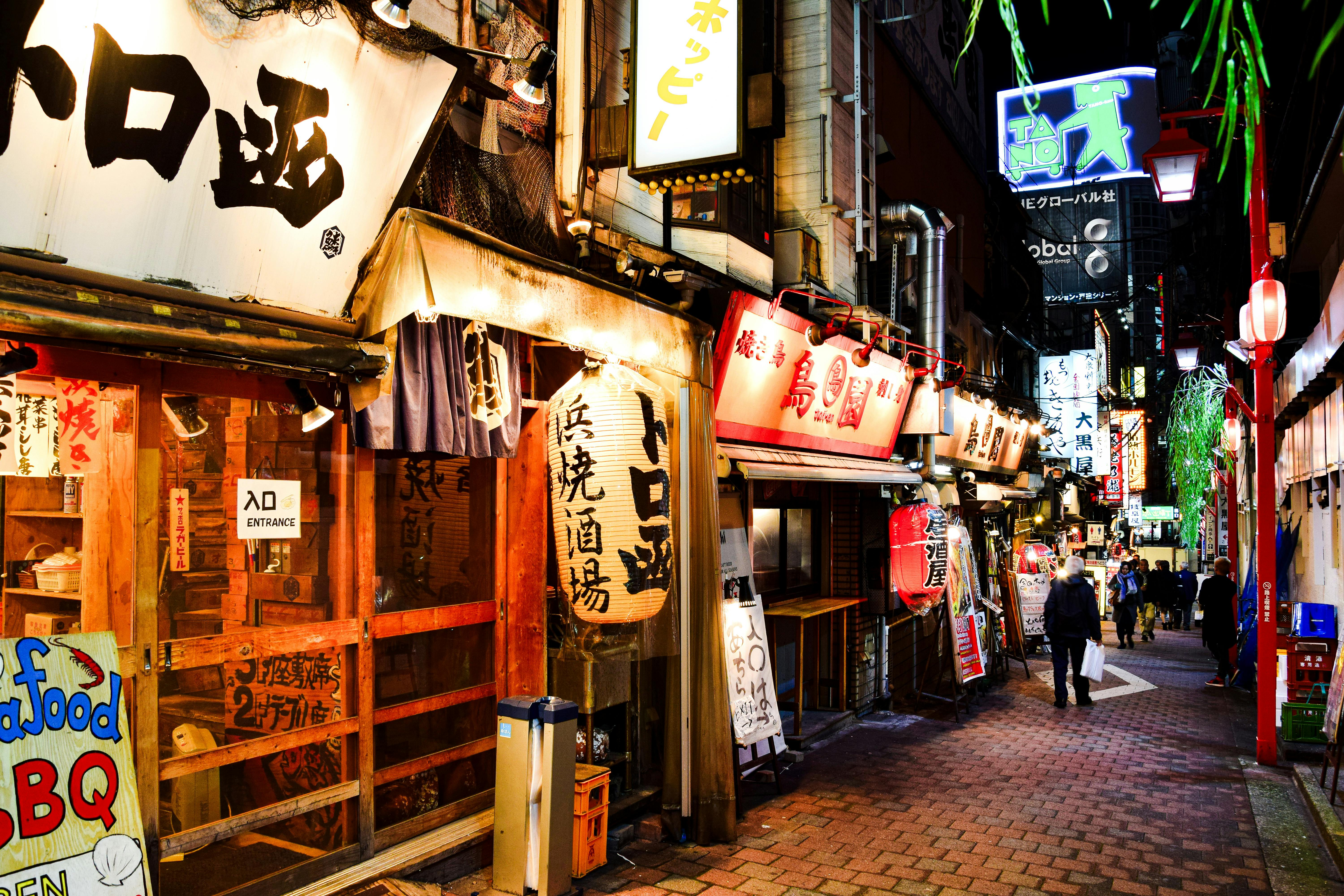 Explore the bustling atmosphere of Shinjuku's illuminated alley filled with cafes and shops during night in Tokyo.