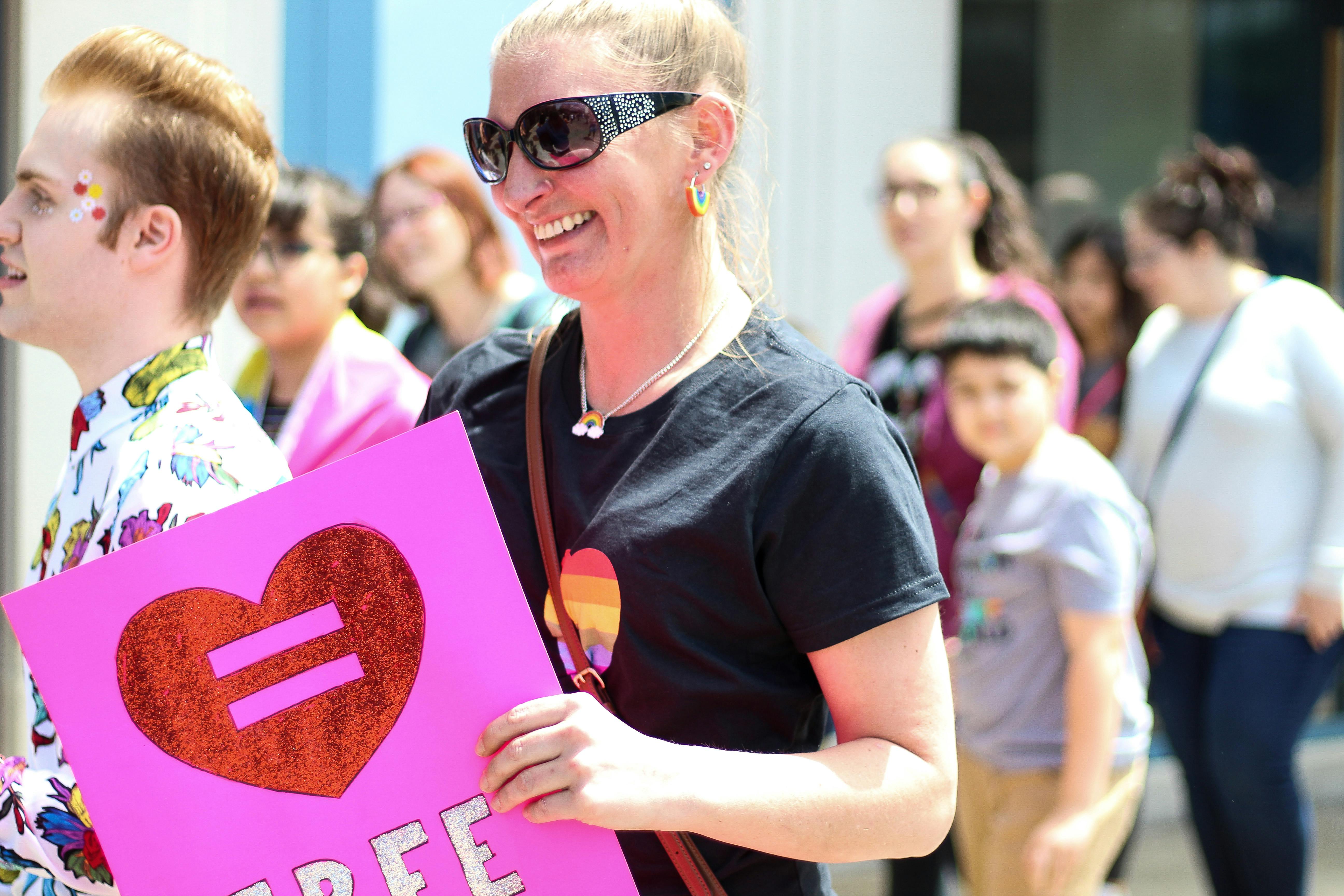 Diverse crowd celebrating LGBTQ+ equality with vibrant signs and smiles in a colorful outdoor parade.