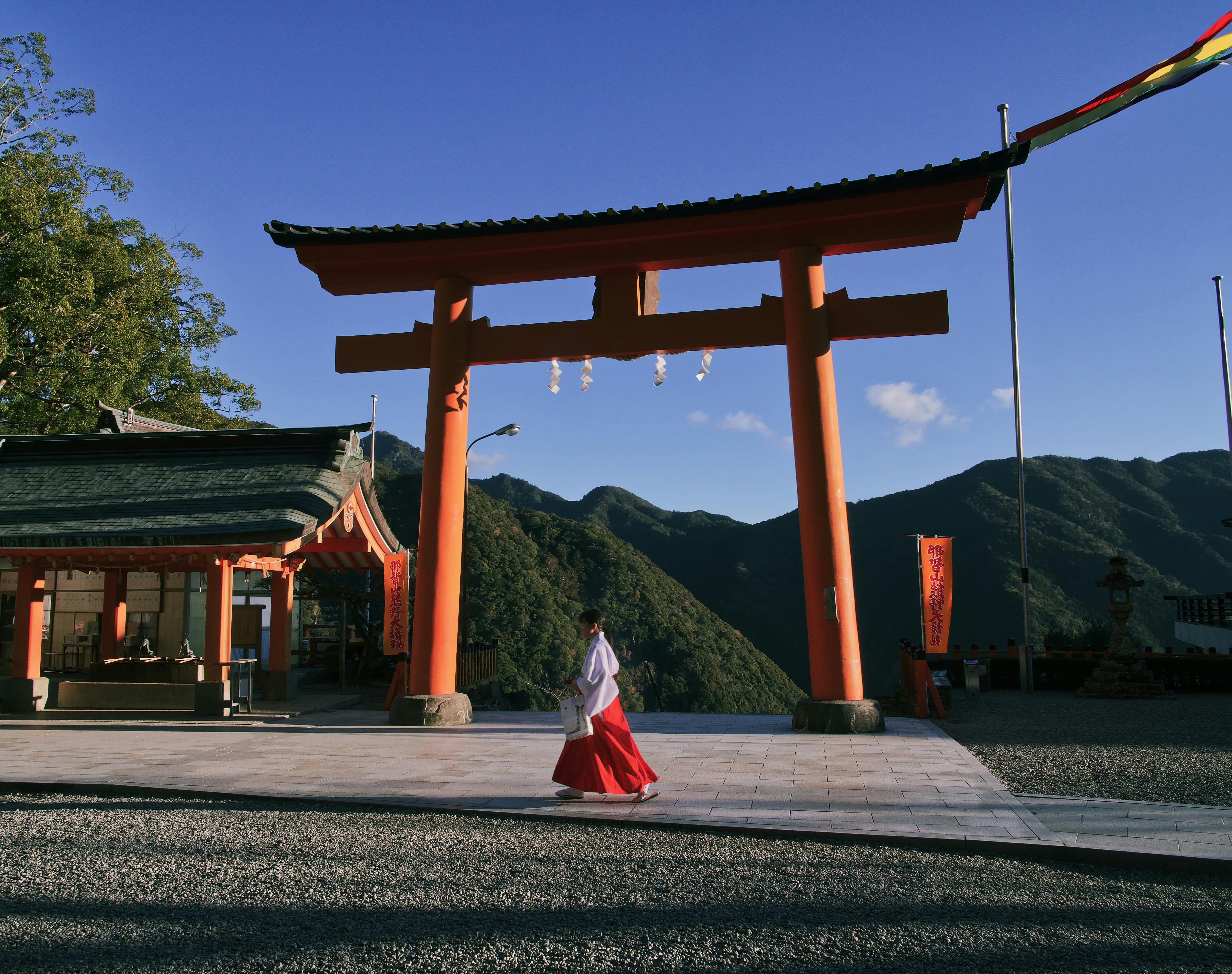 Woman walks through a traditional Shinto torii gate at a serene shrine during daylight.