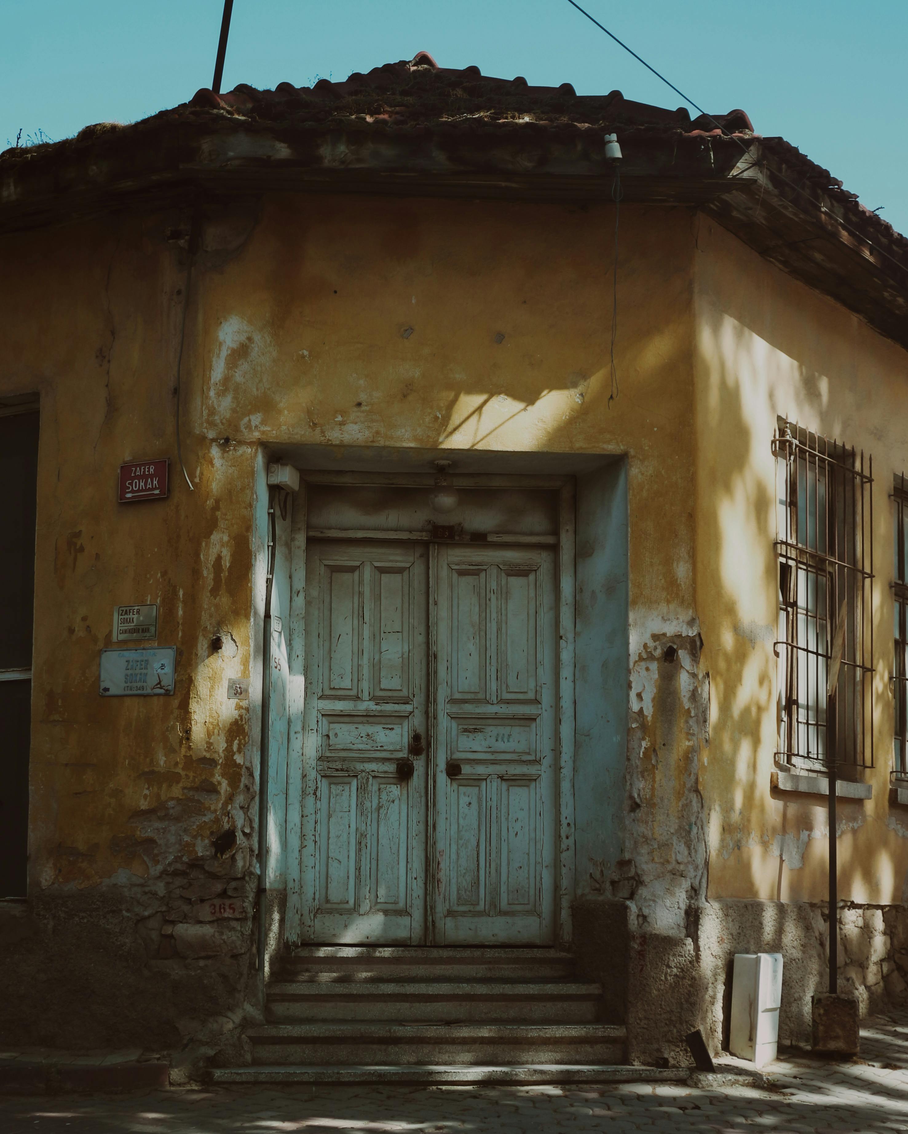 A vintage, abandoned house with cracked paint and wooden doors in a quiet village.