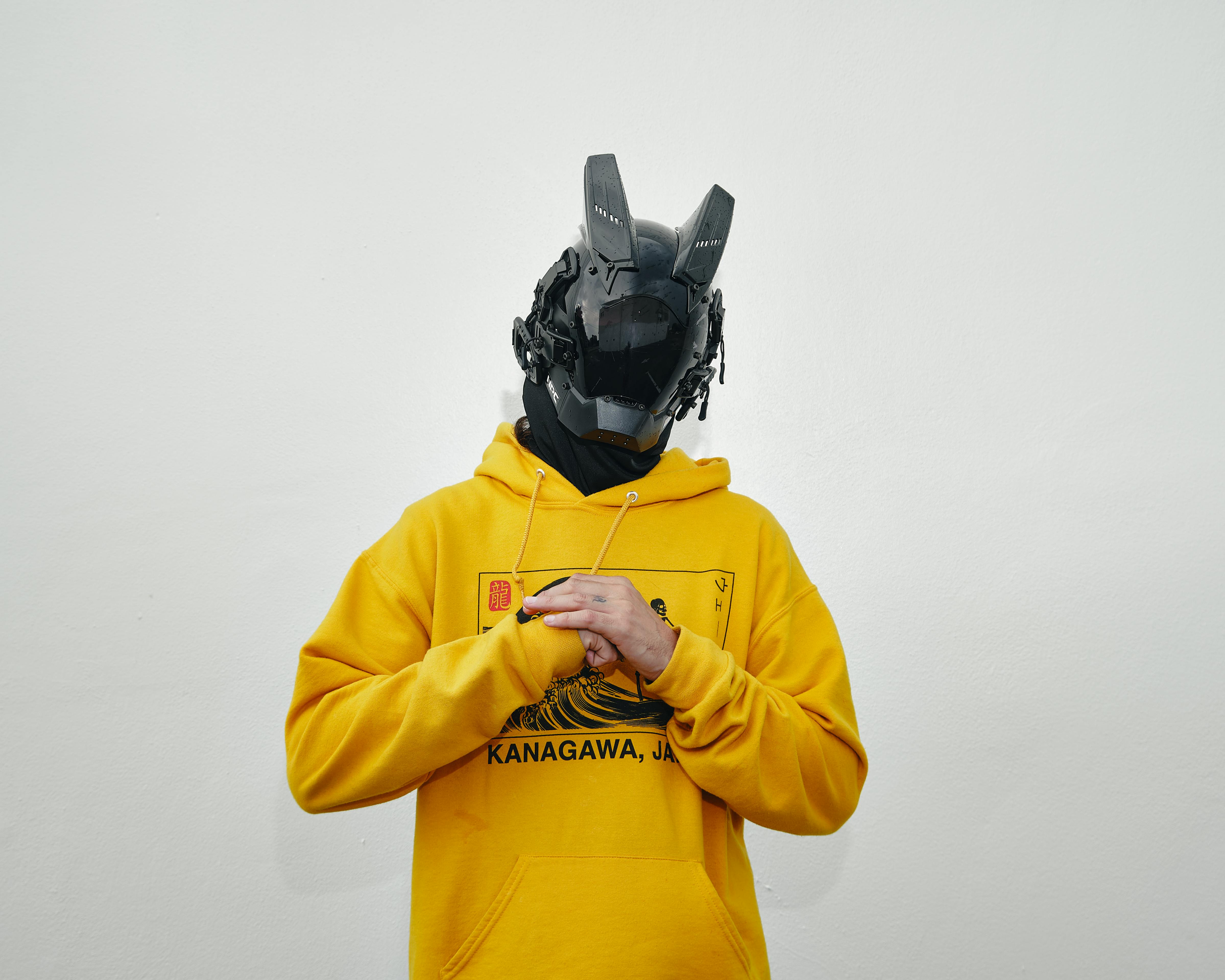 A person in a futuristic mask wearing a yellow hoodie labeled 'Kanagawa, Japan' indoors.