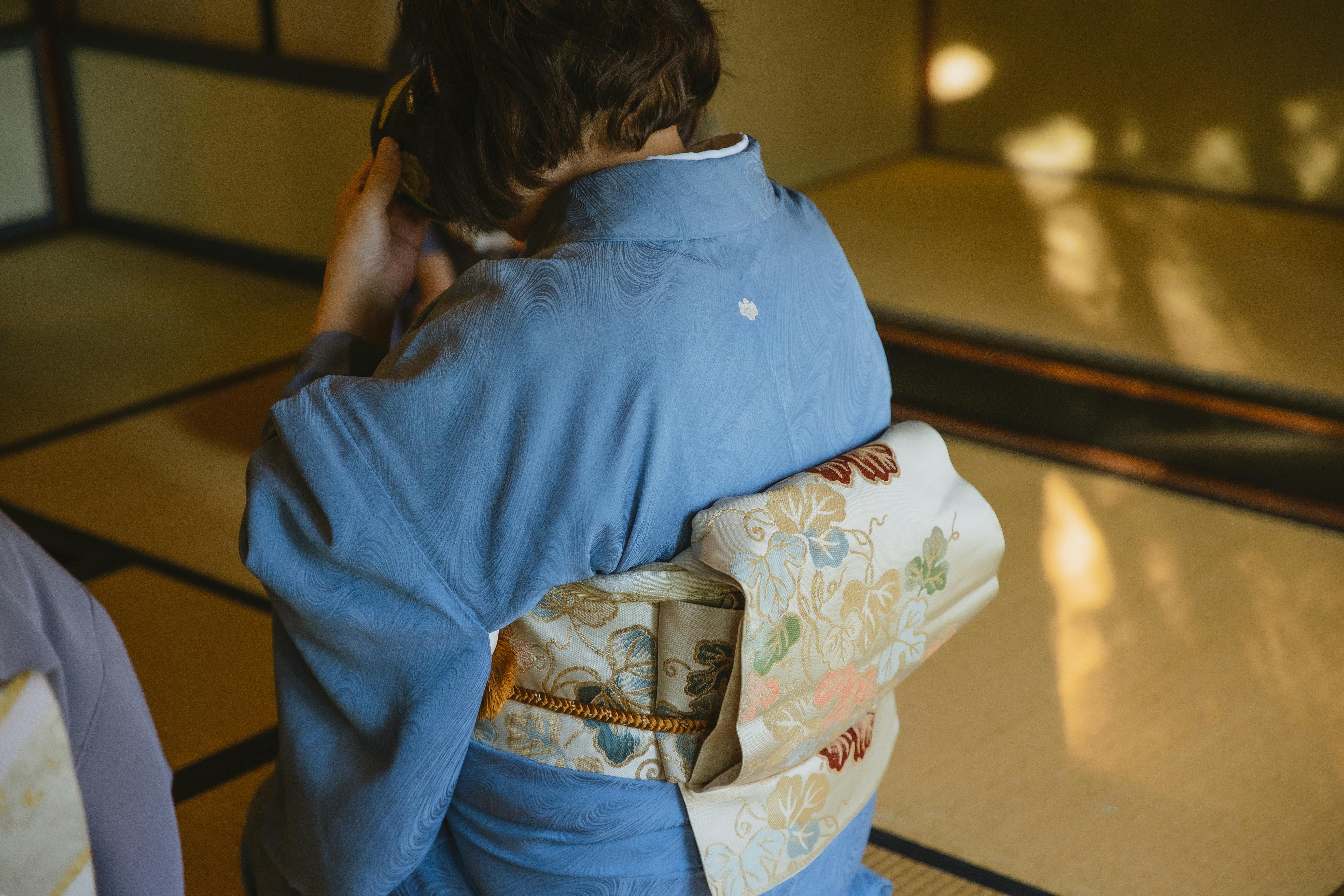 Back view of unrecognizable person wearing authentic robe sitting on tatami while drinking tea from a bowl during a traditional Japanese ceremony