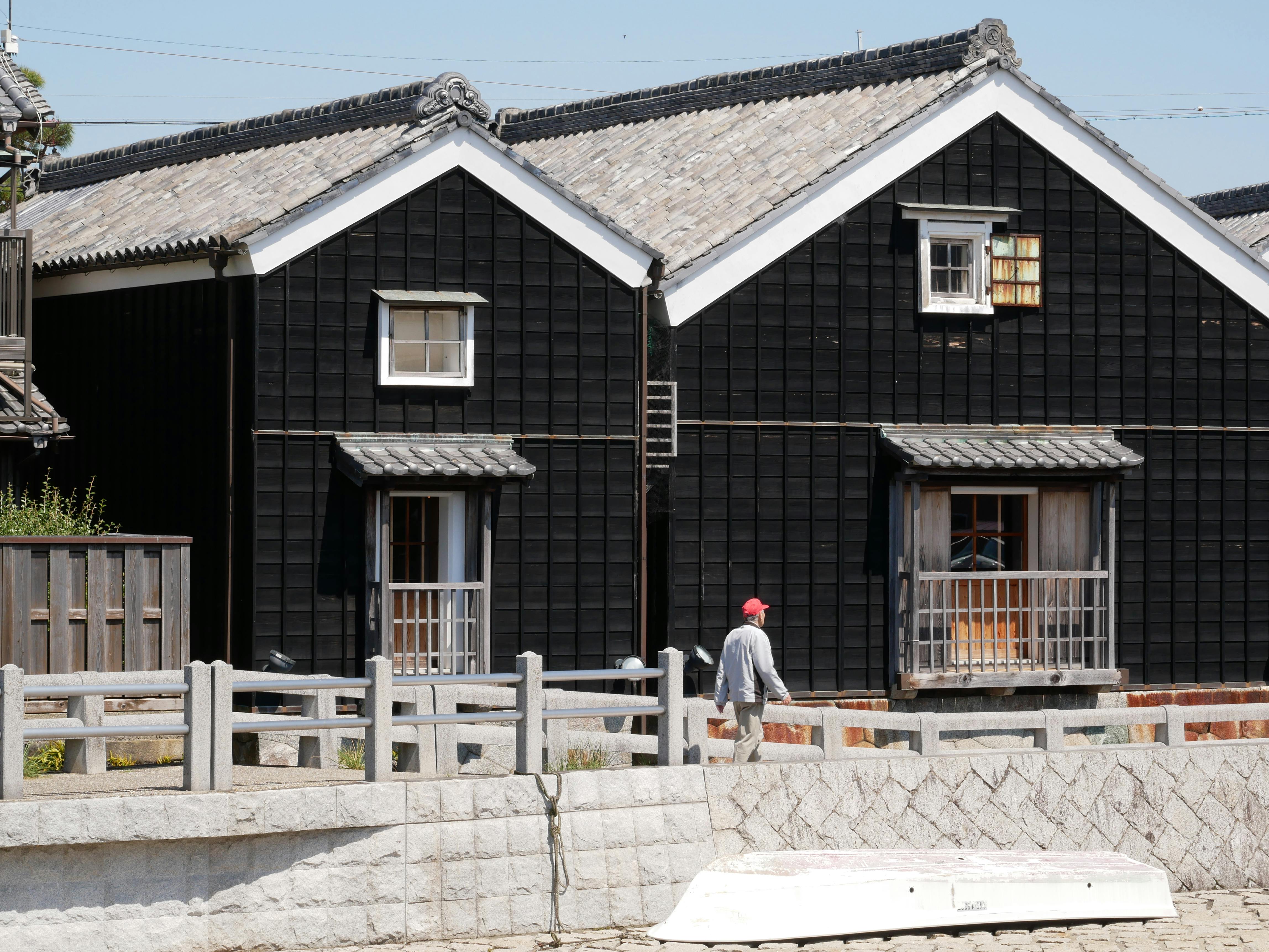 Traditional Japanese wooden buildings in sunlight with a person walking by. Clear day in a residential area.