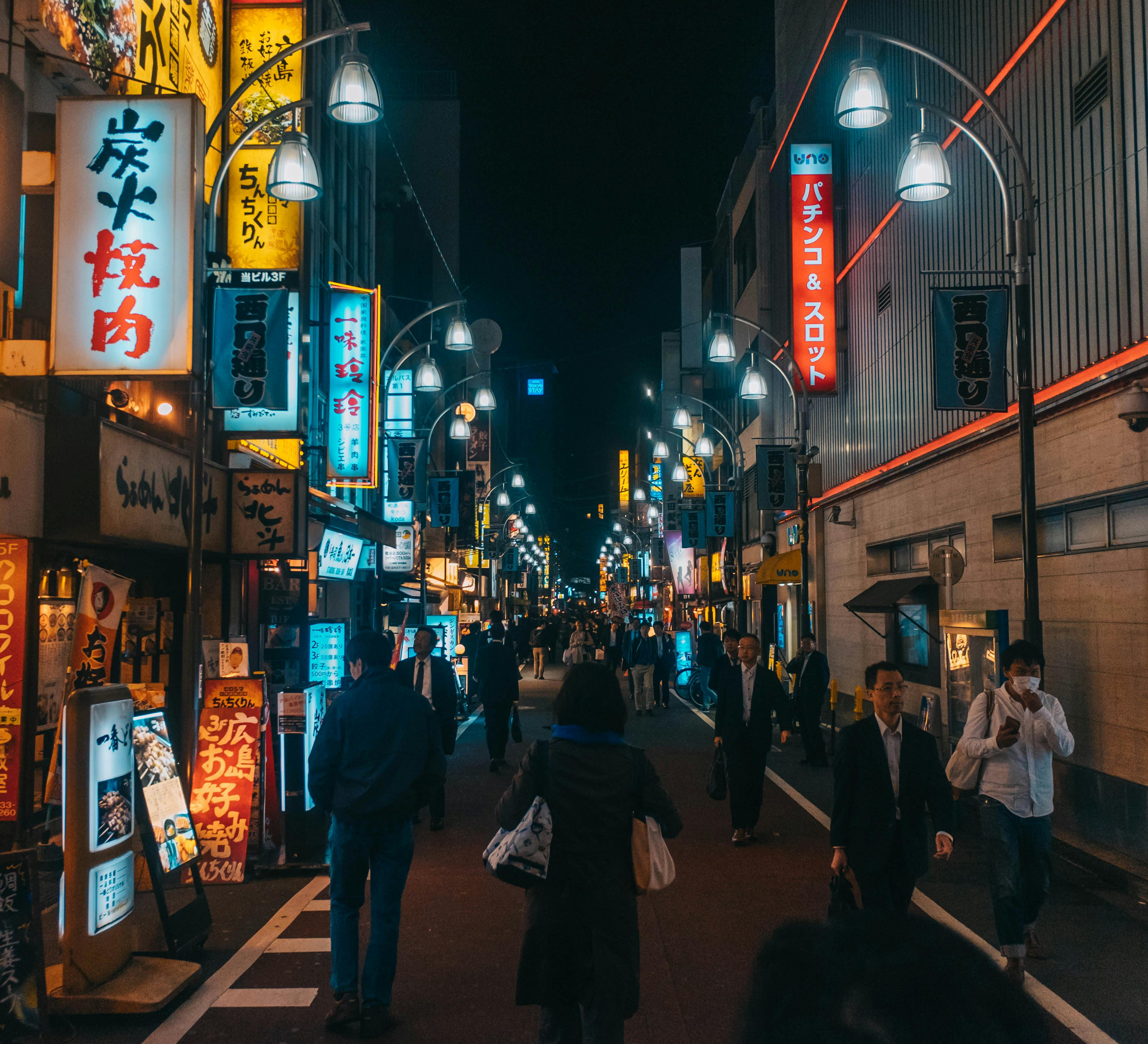 Experience the vibrant energy of Tokyo's nightlife in this bustling urban street scene filled with neon lights and people.