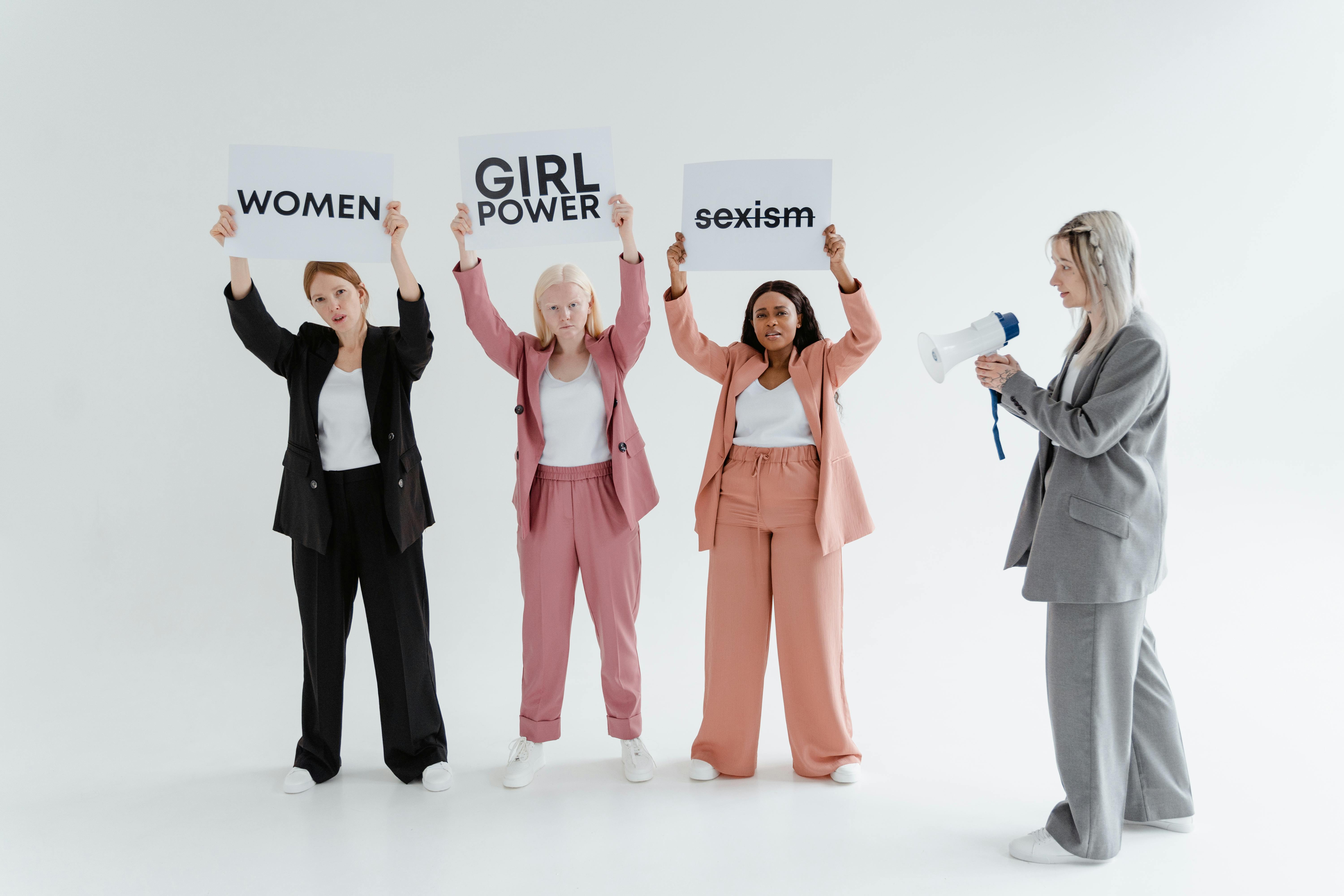 Four women in suits holding signs about girl power and sexism, advocating for equality