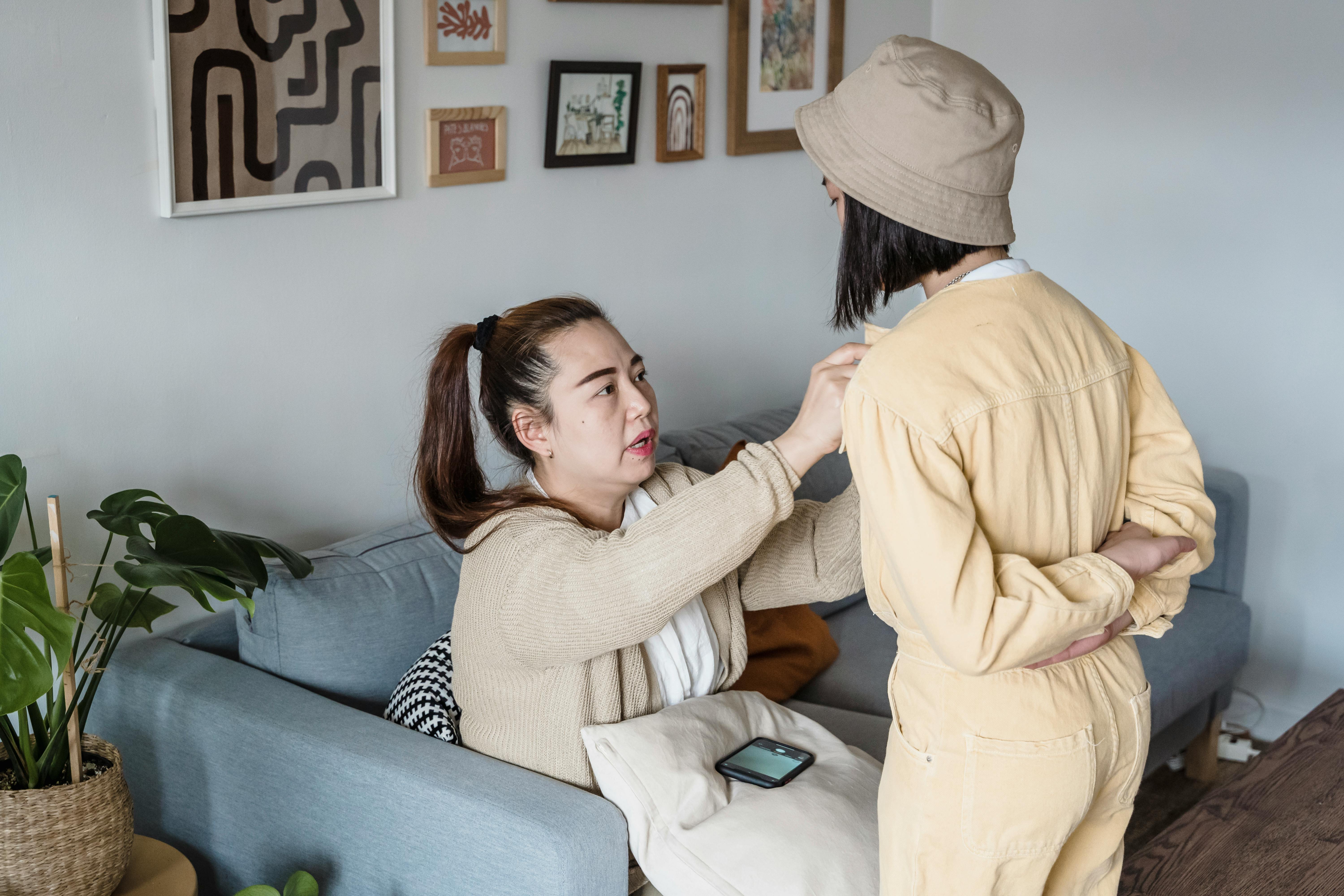 A caring mother helps her daughter with her jacket in a cozy home setting, emphasizing family bonds.