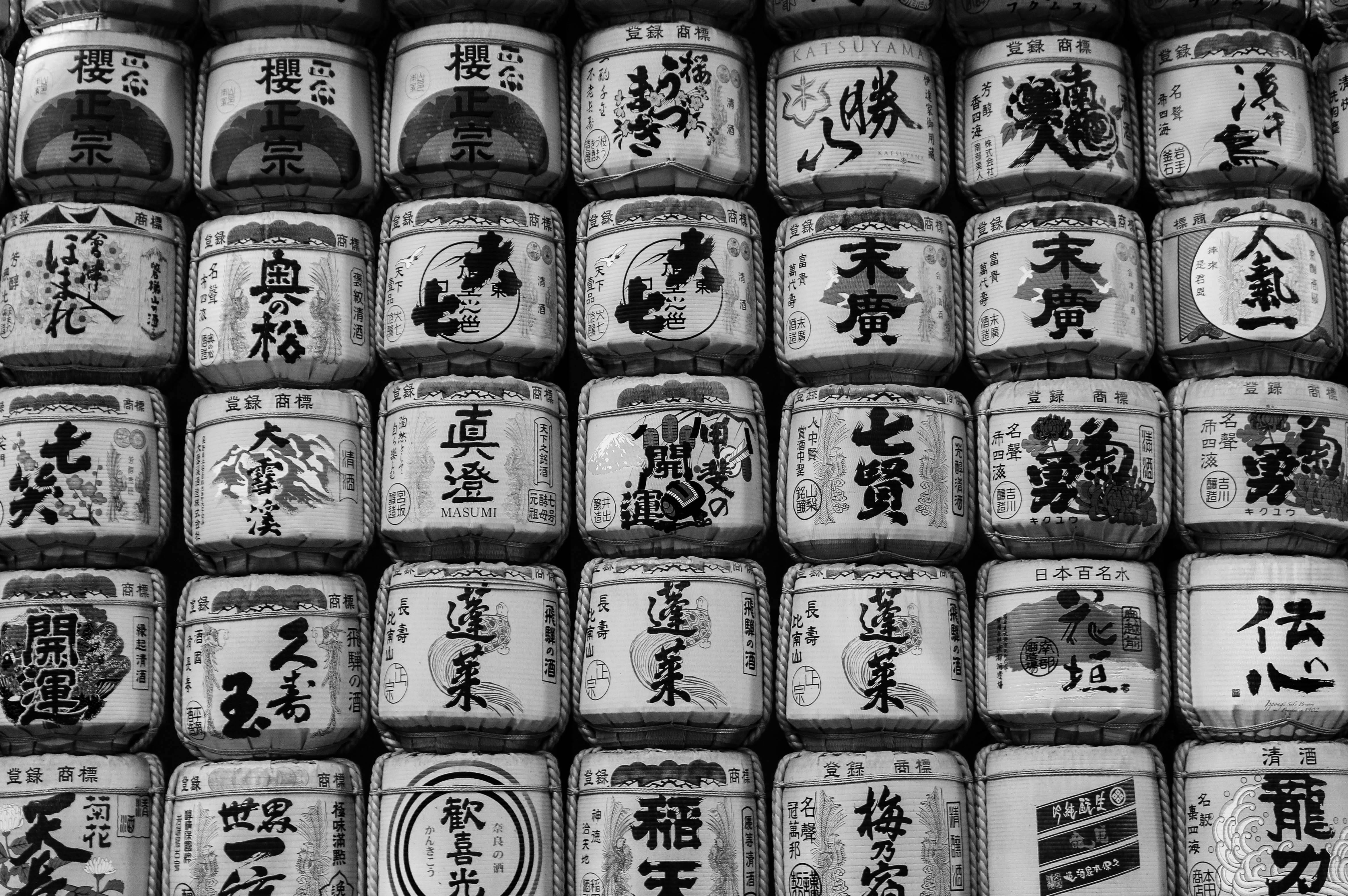 Black and white image of stacked traditional Japanese sake barrels with ornate designs.