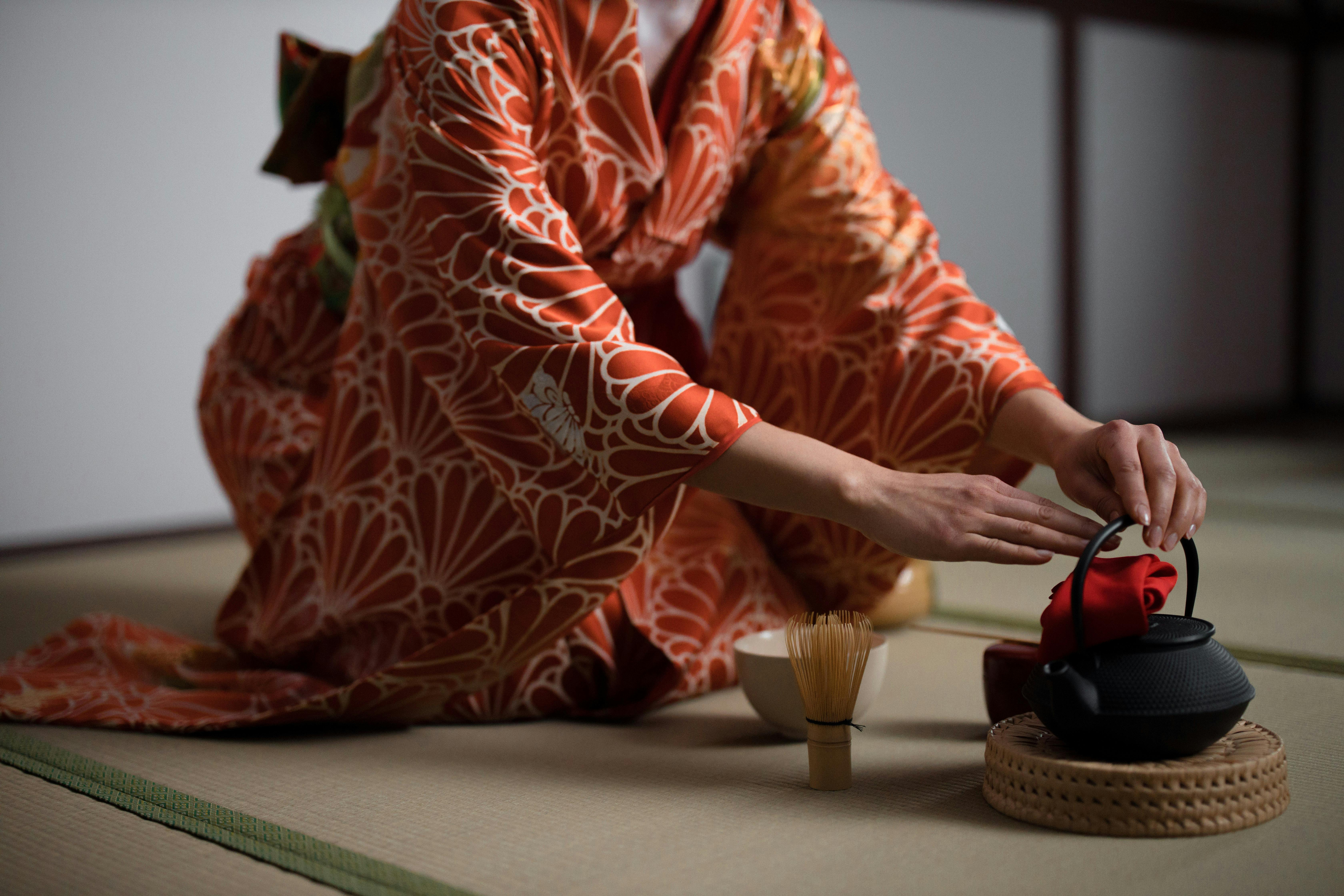 Close-up of a woman in kimono preparing for a Japanese tea ceremony indoors.