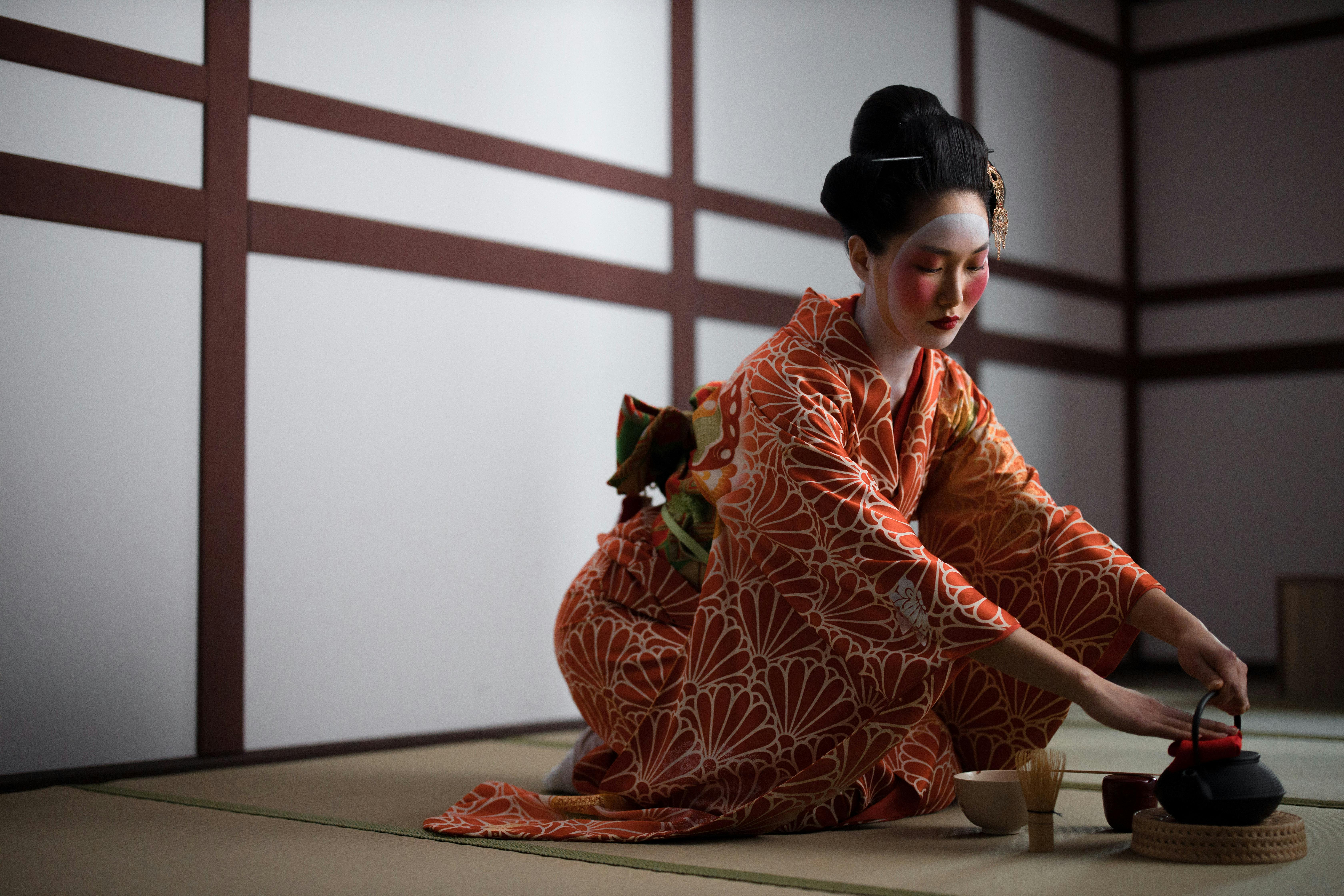 A woman in a kimono performing a traditional Japanese tea ceremony indoors.